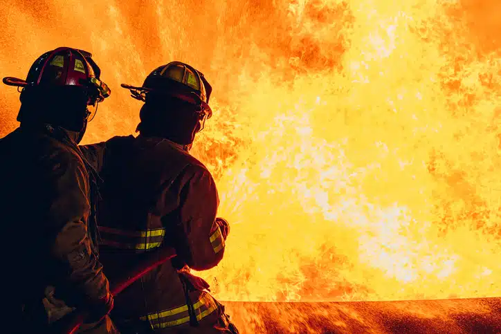 The shadows of two firefighters facing a fire trying to prevent further fire damage through their firefighting efforts.